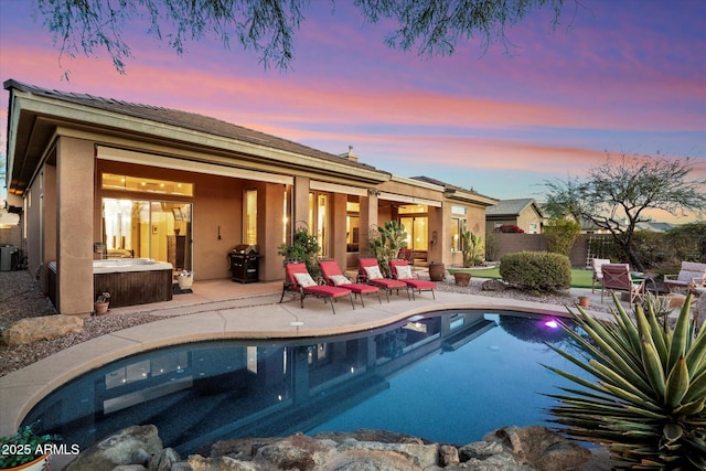 pool at dusk with grilling area and a patio