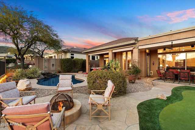 patio terrace at dusk with ceiling fan, an outdoor fire pit, and a fenced in pool