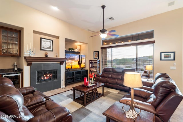 living room with a tiled fireplace, bar, beverage cooler, and ceiling fan