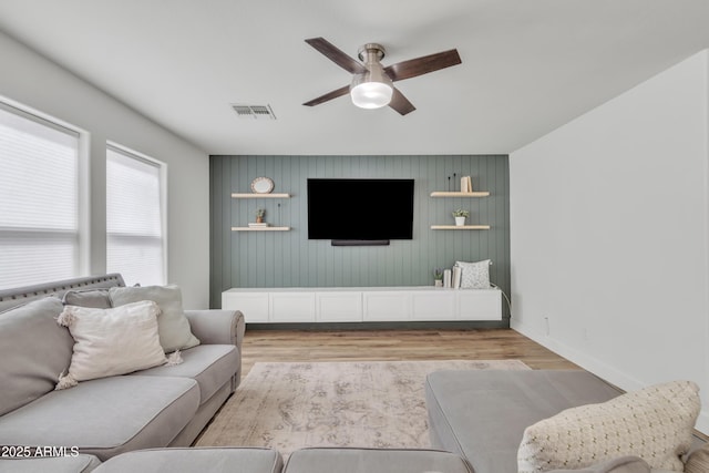 living area featuring light wood-style floors, visible vents, baseboards, and a ceiling fan