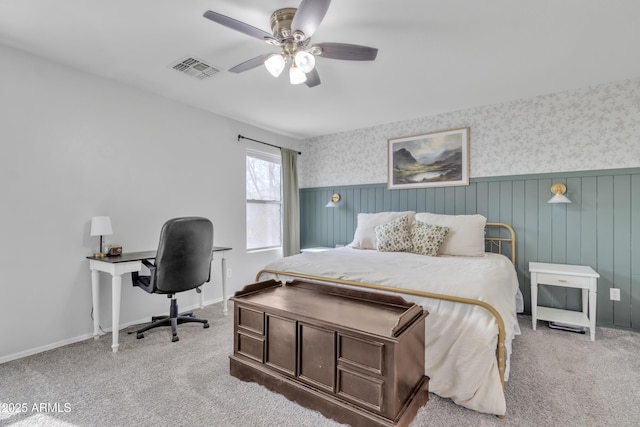 carpeted bedroom with wallpapered walls, visible vents, baseboards, a wainscoted wall, and ceiling fan