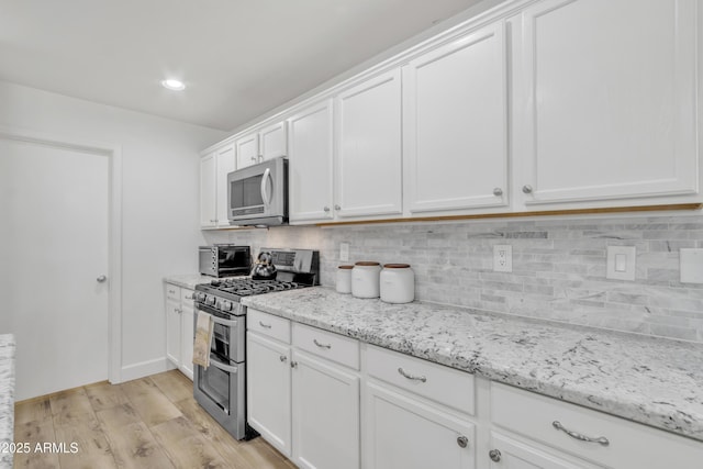 kitchen with light wood finished floors, tasteful backsplash, white cabinets, appliances with stainless steel finishes, and light stone countertops