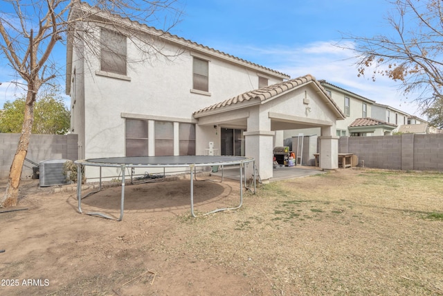 back of house with a trampoline, a fenced backyard, central AC, and stucco siding