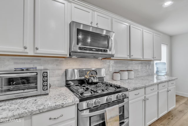 kitchen featuring appliances with stainless steel finishes, tasteful backsplash, a toaster, and white cabinetry