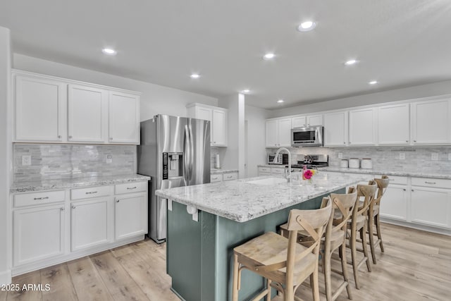 kitchen featuring stainless steel appliances, white cabinets, a sink, an island with sink, and light wood-type flooring