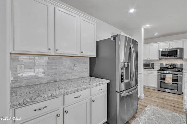 kitchen with appliances with stainless steel finishes, white cabinetry, and light wood-style floors