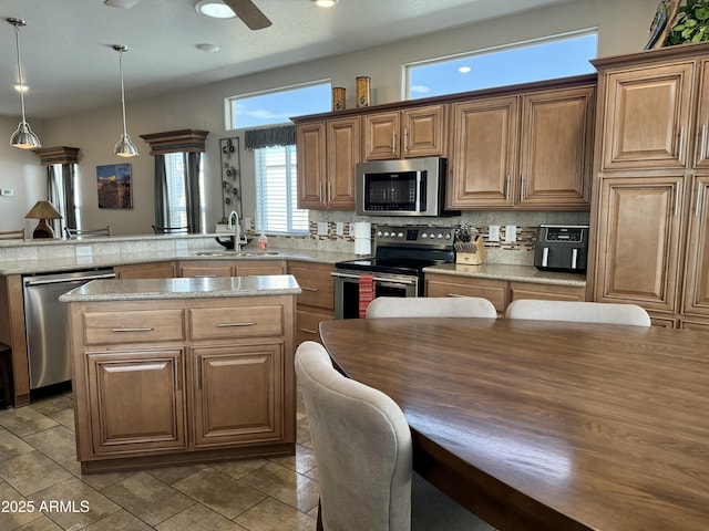 kitchen with decorative backsplash, light stone counters, stainless steel appliances, sink, and pendant lighting