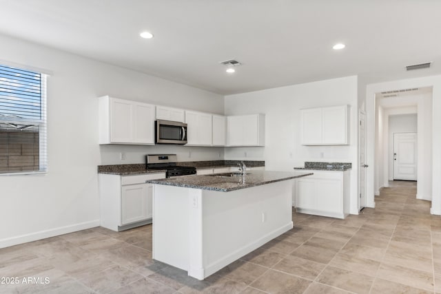 kitchen featuring appliances with stainless steel finishes, white cabinets, dark stone countertops, sink, and a center island with sink