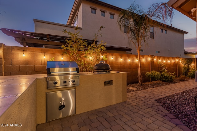 patio terrace at dusk featuring an outdoor kitchen and a grill