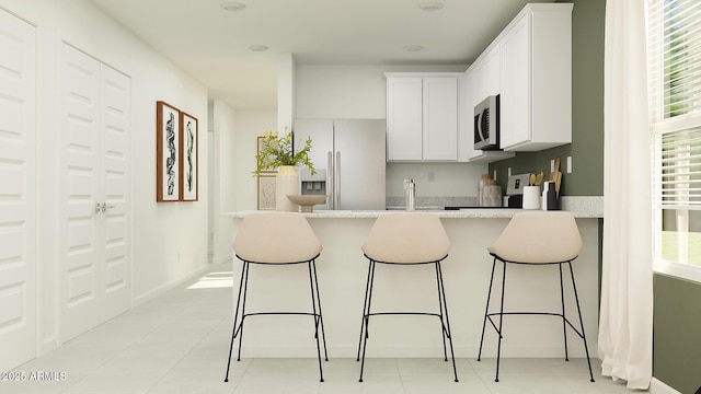 kitchen featuring a peninsula, stainless steel microwave, refrigerator with ice dispenser, and white cabinets