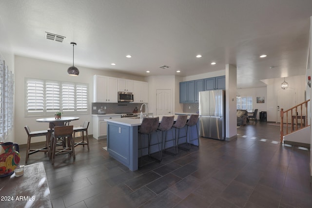 kitchen with appliances with stainless steel finishes, white cabinetry, a kitchen island with sink, blue cabinets, and decorative light fixtures