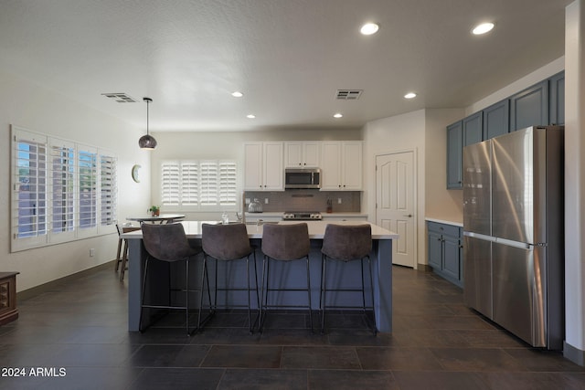 kitchen with tasteful backsplash, appliances with stainless steel finishes, white cabinetry, a kitchen island with sink, and pendant lighting