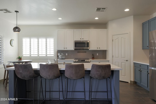 kitchen featuring a kitchen island with sink, appliances with stainless steel finishes, decorative light fixtures, and white cabinets