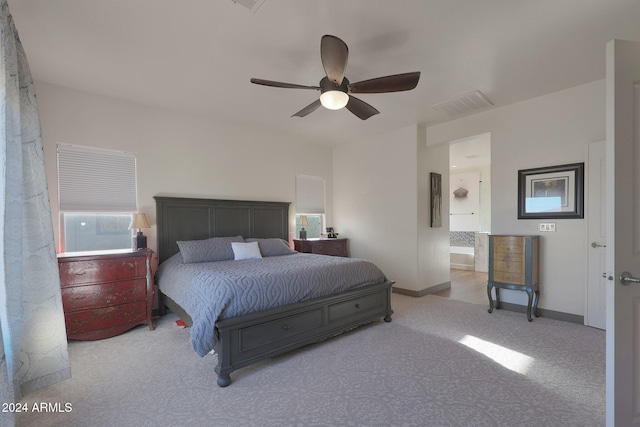 bedroom featuring light carpet, ensuite bathroom, and ceiling fan