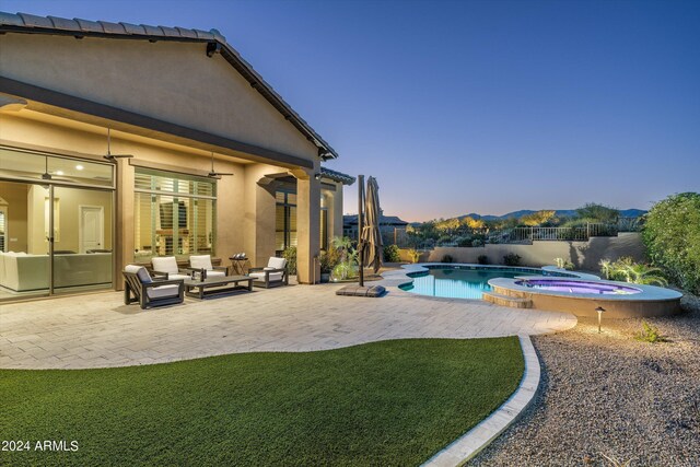 pool at dusk with a yard, a patio, outdoor lounge area, and an in ground hot tub