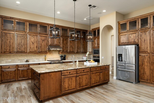 kitchen with a center island with sink, backsplash, stainless steel appliances, and light wood-type flooring