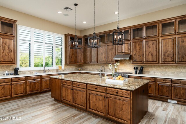 kitchen with a notable chandelier, stainless steel stove, backsplash, light hardwood / wood-style floors, and a kitchen island with sink