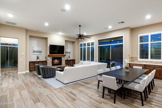 living room featuring ceiling fan, light hardwood / wood-style floors, and a stone fireplace