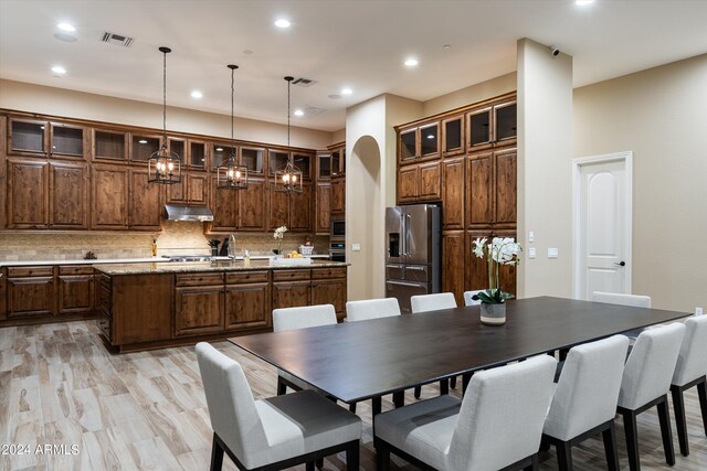 kitchen featuring decorative light fixtures, a center island with sink, light hardwood / wood-style floors, stainless steel appliances, and decorative backsplash