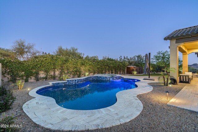 pool at dusk with a patio area and an in ground hot tub