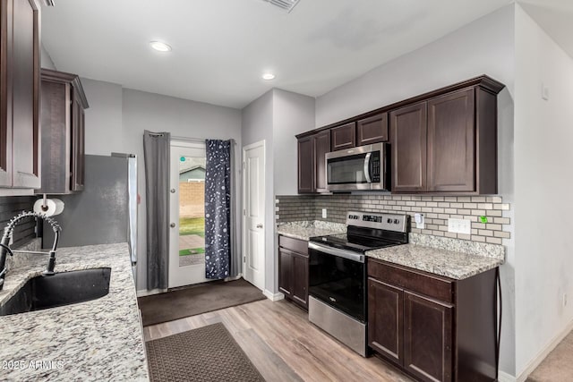 kitchen with dark brown cabinetry, appliances with stainless steel finishes, decorative backsplash, and a sink