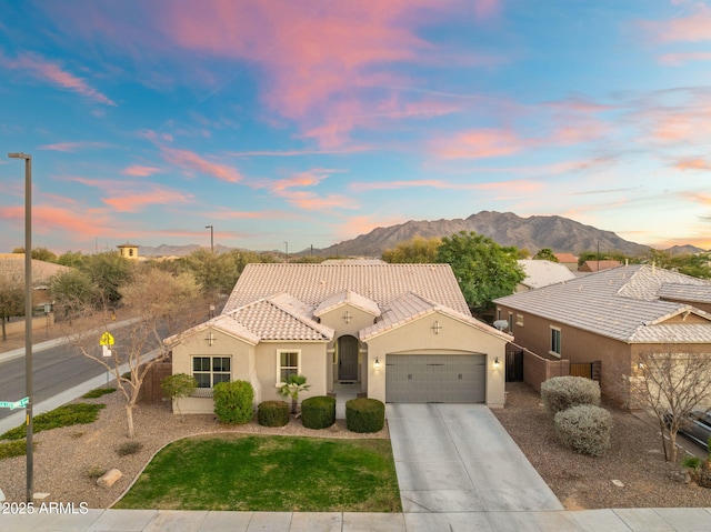 view of front of property featuring an attached garage, a mountain view, a tiled roof, driveway, and stucco siding