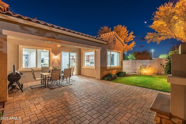 patio at night featuring outdoor dining area, fence, and a lawn