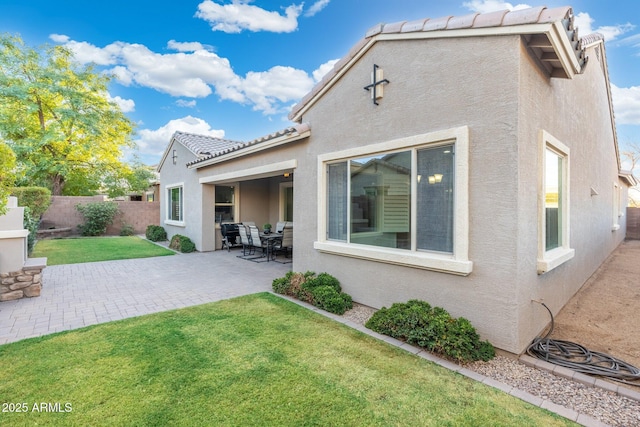 rear view of property featuring a patio, fence, a yard, a tiled roof, and stucco siding