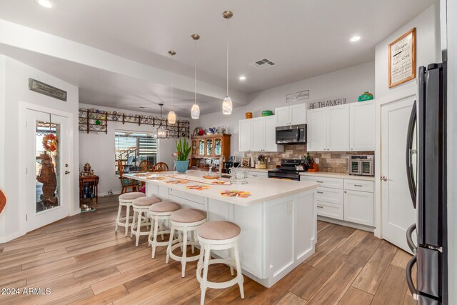 kitchen featuring a center island with sink, white cabinets, hanging light fixtures, light hardwood / wood-style flooring, and stainless steel appliances