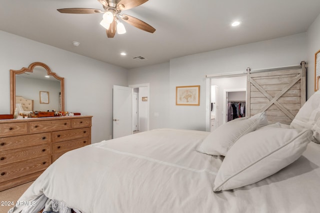 carpeted bedroom with a barn door, a walk in closet, a closet, and ceiling fan