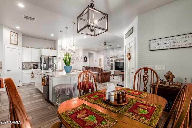 dining area featuring hardwood / wood-style floors, ceiling fan with notable chandelier, and sink