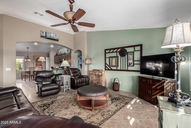 living area featuring light tile patterned floors, visible vents, arched walkways, and a ceiling fan