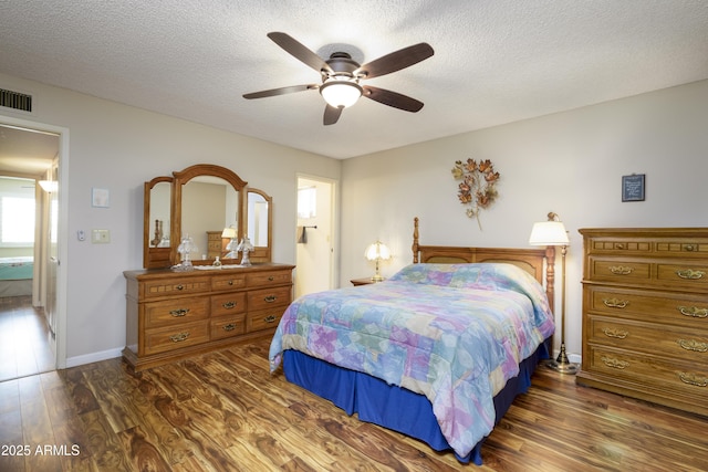 bedroom featuring a textured ceiling, a ceiling fan, visible vents, baseboards, and dark wood-style floors