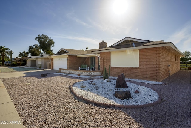 ranch-style house with concrete driveway, brick siding, a chimney, and an attached garage