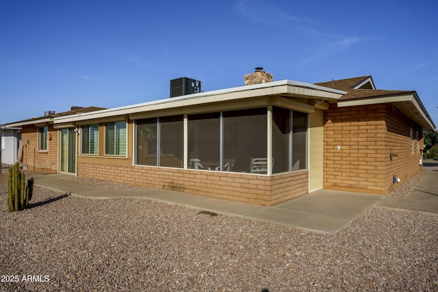 back of house with a sunroom, brick siding, a chimney, and central air condition unit