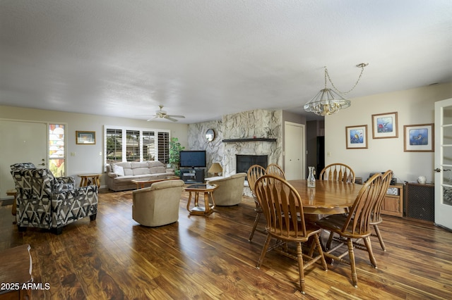 dining area featuring dark wood-style floors, ceiling fan with notable chandelier, and a fireplace