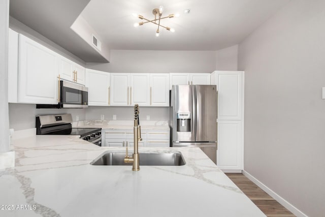 5303 N 7th St Unit 326, Phoenix, AZ 85014 - kitchen featuring stainless steel appliances, wood finished floors, light stone countertops, white cabinetry, and a chandelier