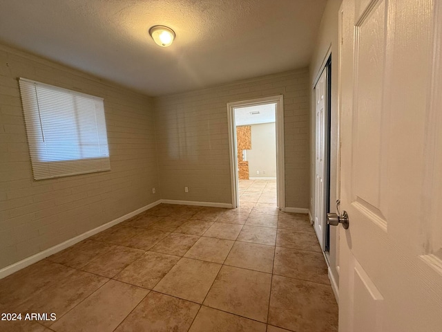 tiled spare room featuring a textured ceiling and brick wall