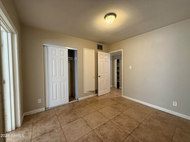 unfurnished bedroom featuring a closet, light tile patterned floors, and a textured ceiling