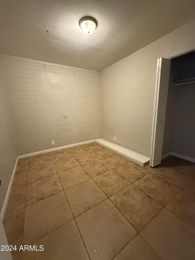 interior space featuring a textured ceiling, tile patterned floors, and brick wall