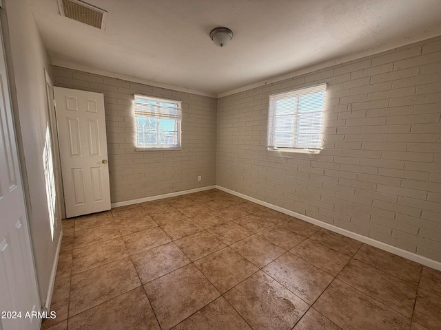 unfurnished room featuring brick wall, light tile patterned floors, and a healthy amount of sunlight