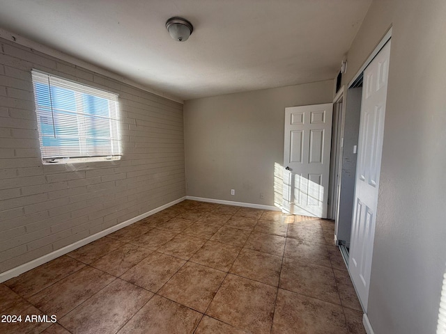 unfurnished room with tile patterned floors and brick wall