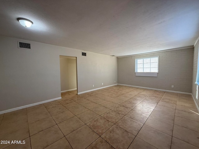 empty room featuring light tile patterned floors, a textured ceiling, and brick wall