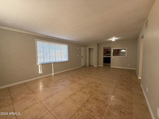 tiled empty room featuring brick wall and a textured ceiling