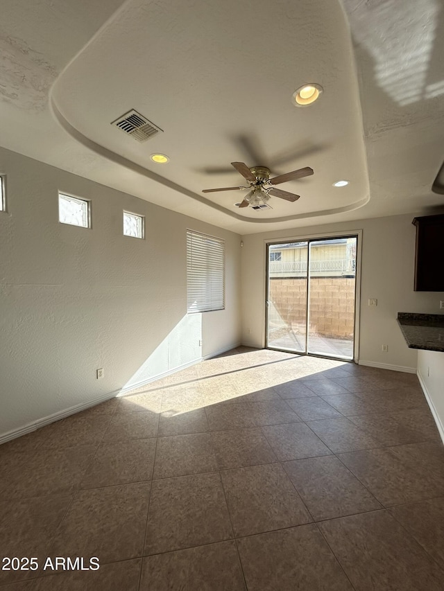 empty room featuring a raised ceiling, dark tile patterned floors, and ceiling fan