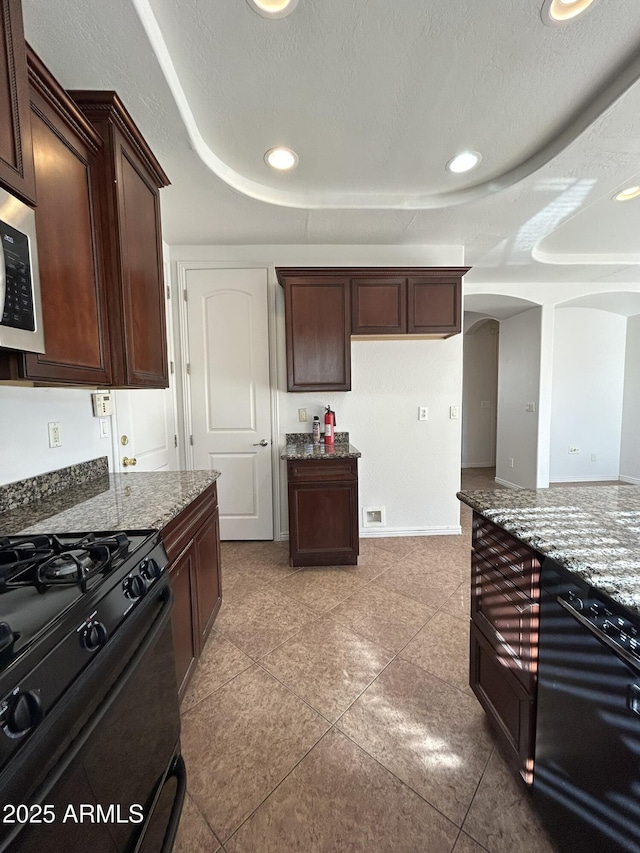 kitchen with light tile patterned flooring, light stone countertops, dark brown cabinets, and black gas range