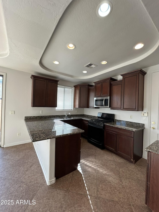 kitchen with dark brown cabinetry, a textured ceiling, black gas range oven, a raised ceiling, and tile patterned flooring