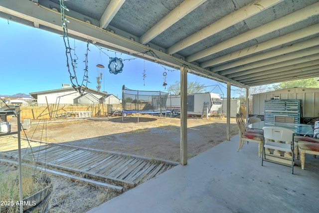 view of patio with a trampoline, fence, a storage shed, an outdoor structure, and outdoor dining space