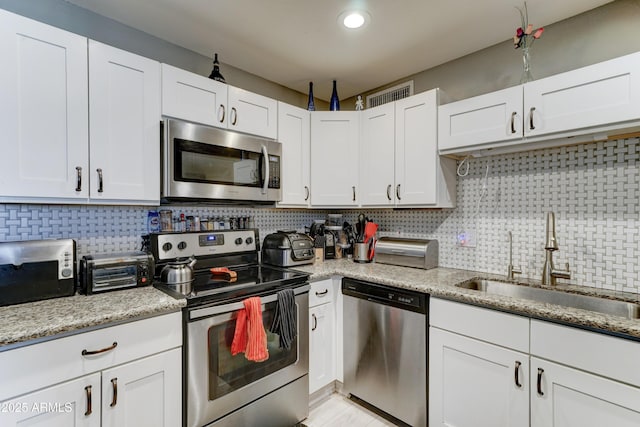 kitchen with decorative backsplash, white cabinets, stainless steel appliances, and a sink