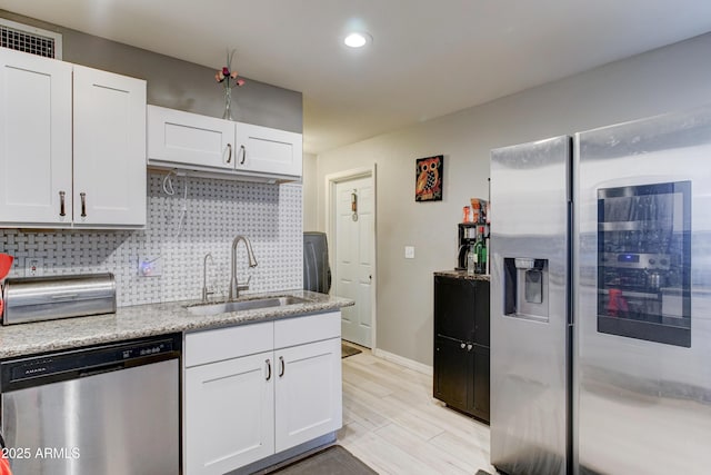 kitchen featuring tasteful backsplash, dishwasher, light wood-type flooring, white cabinets, and a sink